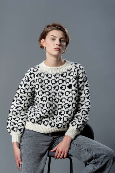 Handmade wool sweater with cropped cut and puffed sleeves. On the sweater is a herd of white sheep going all around, a single black sheep is on the front top left of the sweater.